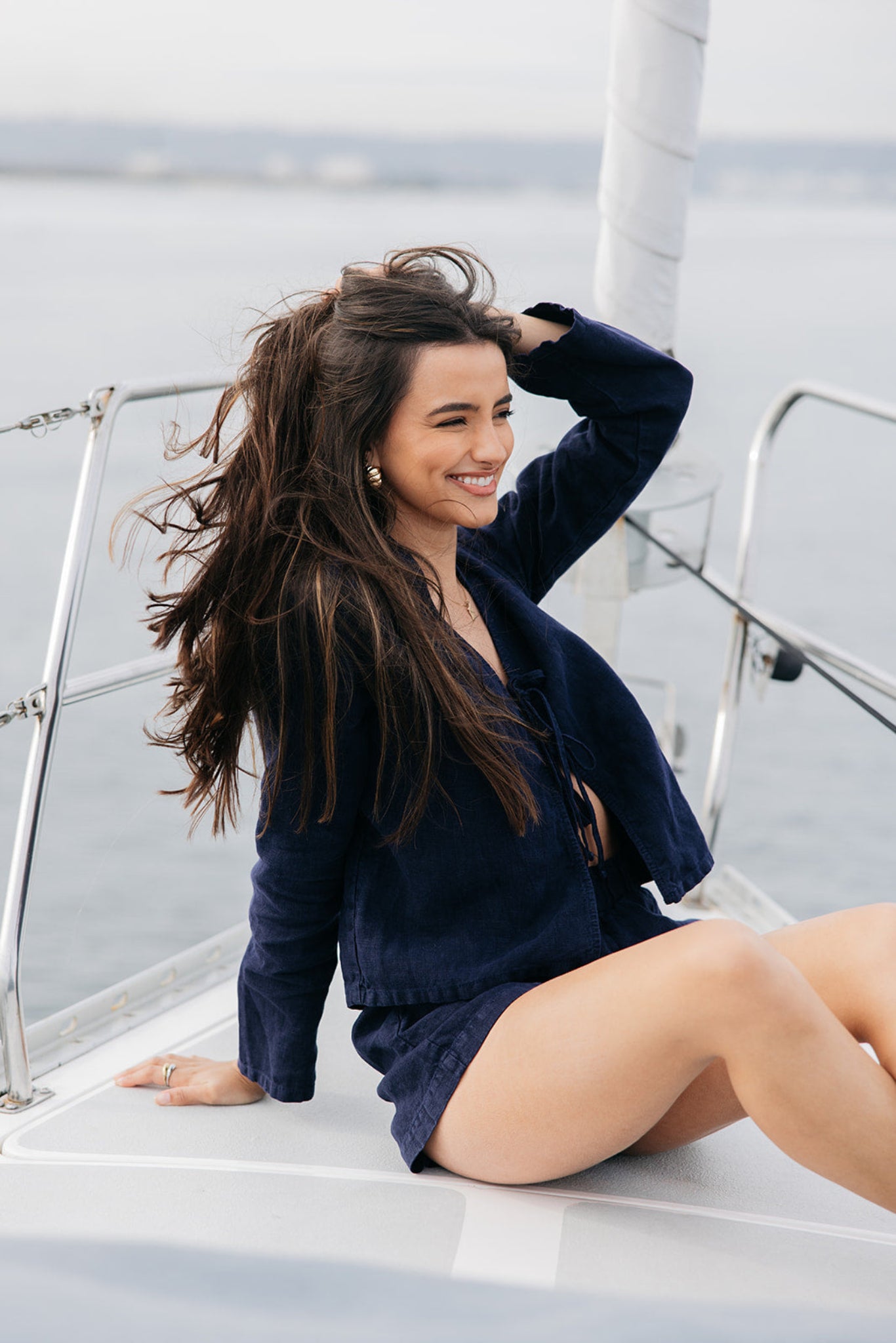 Model wearing Hudson Linen Shorts in navy | linen | styled with gold jewelry and matching Keaton Tie Top | on a sailboat