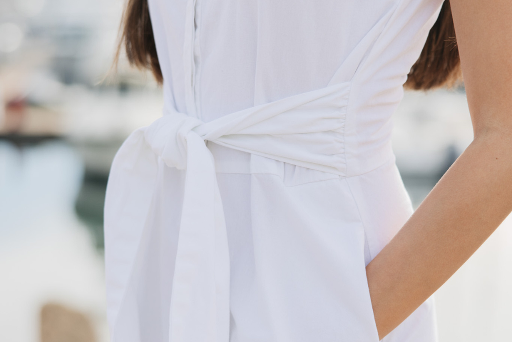 A girl wearing a timeless white dress with a tie front and pockets