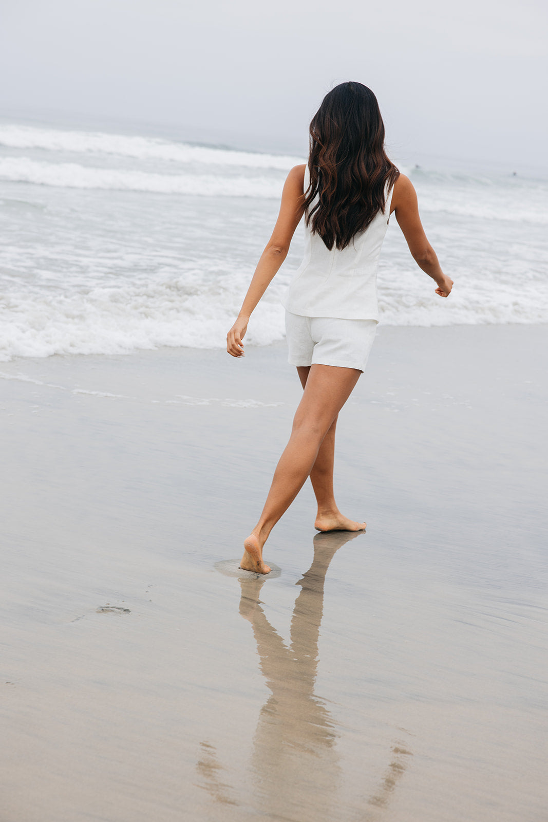 Woman running on the beach wearing tailored white mini shorts made from linen